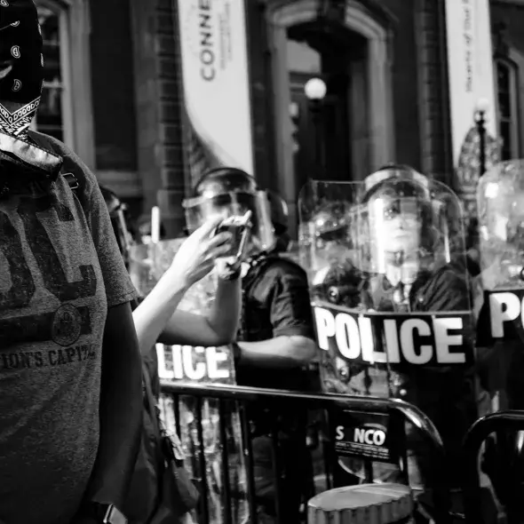 Police in riot gear - protestor in foreground - wearing face mask