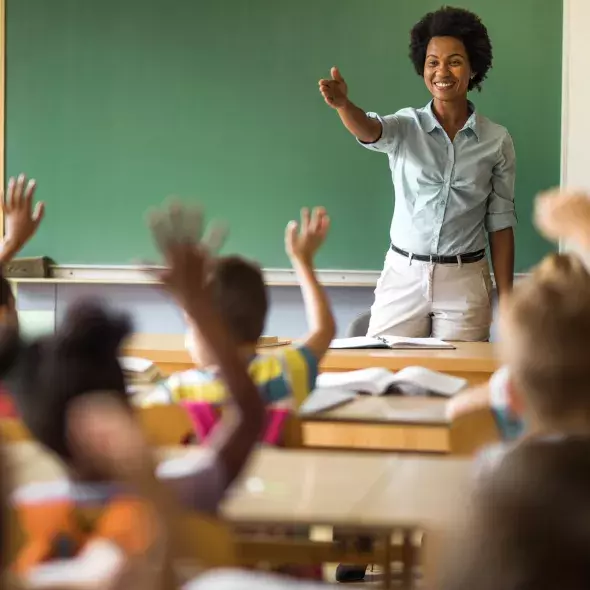 Teacher Standing at Front of Classroom and Calling on Students with Raised Hands