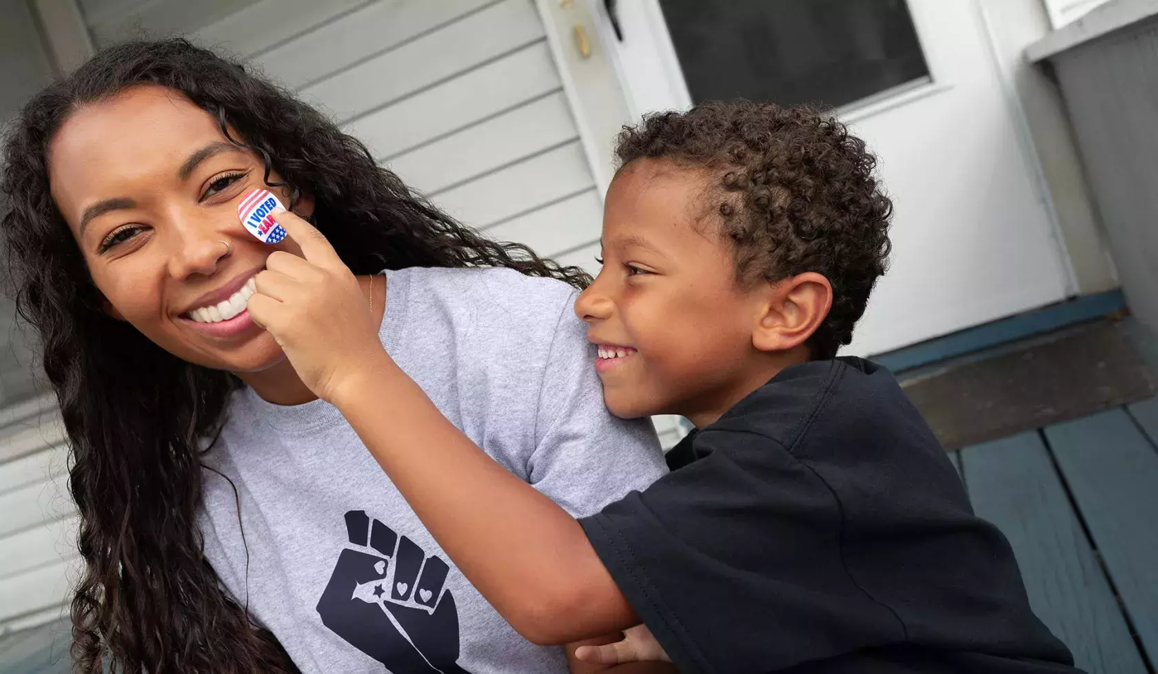 Black Child Putting "I Voted" Sticker on Woman's Cheek - Smiling