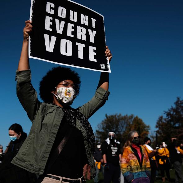 Black Female holding Voting Sign - Group in background - wearing face mask